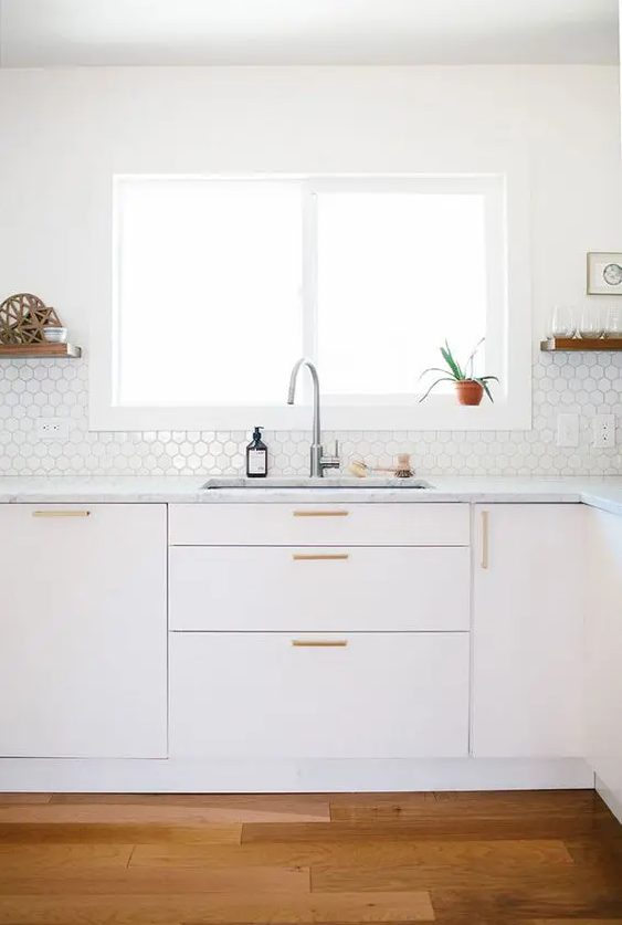 a sleek all-white kitchen with only lower cabinets, a white hex tile backsplash that gives it a bit of interest