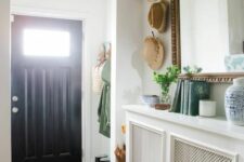 a small yet cool entryway with a radiator covered with screens that doubles as a console table, with books and decor, a large mirror in a chic frame