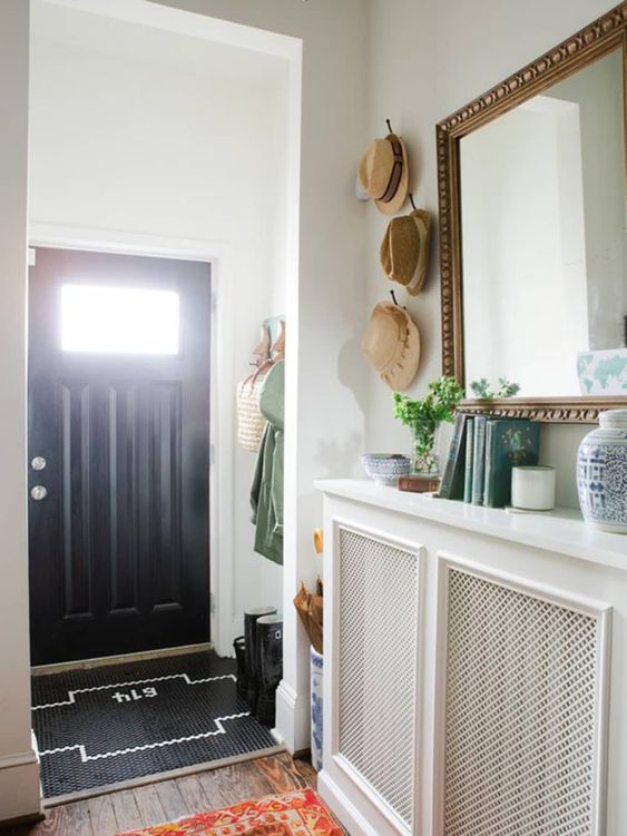 a small yet cool entryway with a radiator covered with screens that doubles as a console table, with books and decor, a large mirror in a chic frame