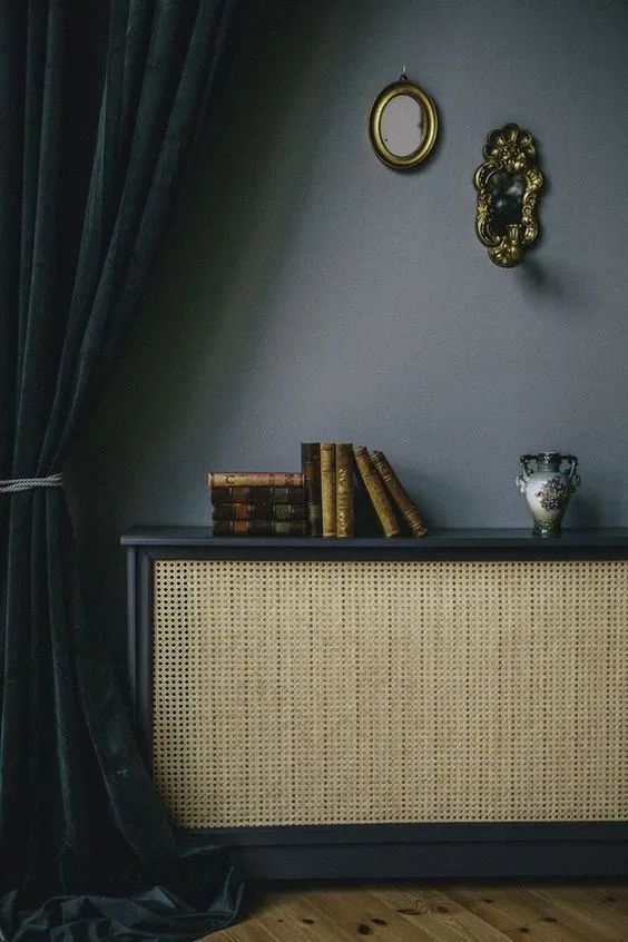 a stylish radiator cover of a black frame with a cane screen turned into a bookshelf with books and some elegant decor