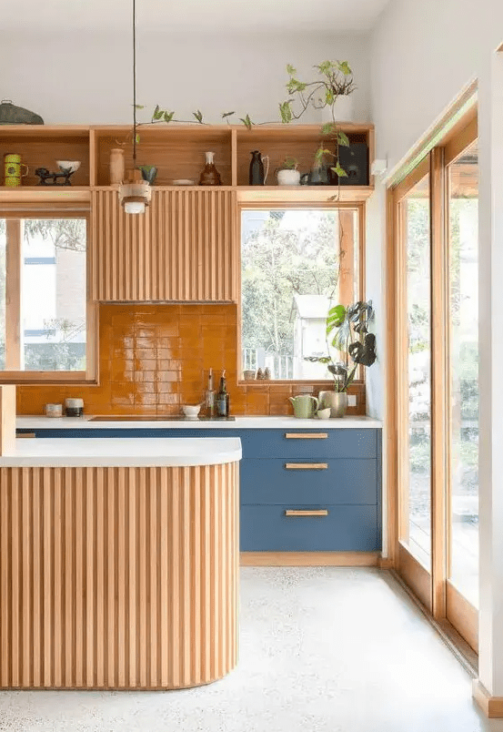 A welcoming warm colored kitchen with blue cabinets, an orange backsplash and some light stained cabinets, a curved kitchen island
