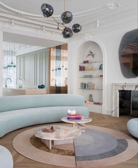 a whimsical living room with a white marble fireplace, built-in shelves, a light blue curved sofa, marble tables and cool rugs