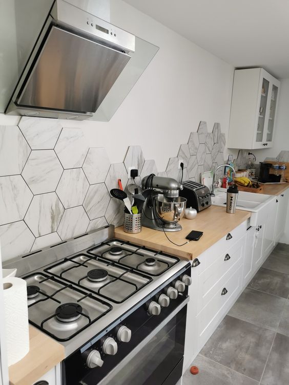 a white Nordic kitchen with butcherblock countertps and a grey hexagon tile backsplash plus butcherblock countertops