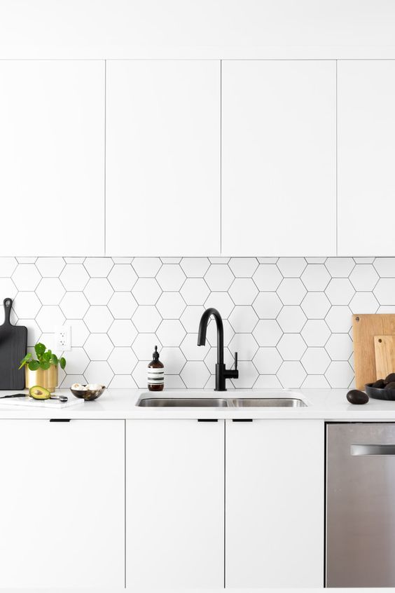 a white Scandinavian kitchen with sleek cabinets, a white hexagon tile backsplash with black grout and black fixtures