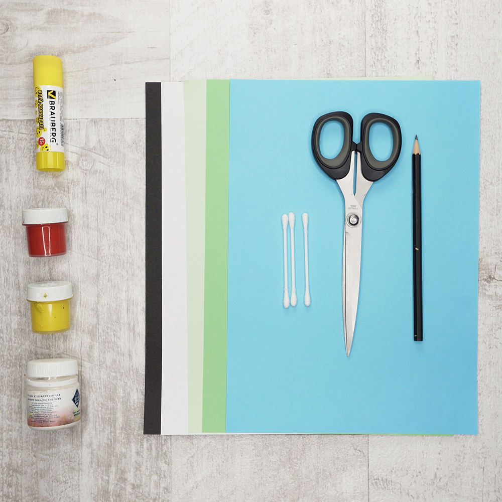 The supplies are colored paper (blue, two shades of green, ivory and black), cotton swabs, scissors, a pencil, a glue stick, red, white and yellow paint.