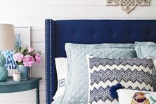 15 a bold blue wingback headboard with a nail trim and bright printed pillows make up a chic look