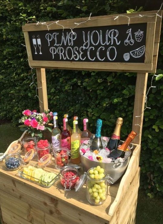 a prosecco bar with a chalkboard sign, prosecco, fruits and berries plus a floral centerpiece