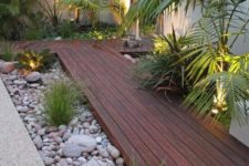 05 a dark stained wooden garden path with large pebbles and rocks plus some greenery and lights around