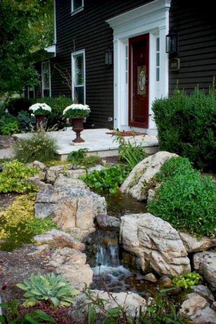 a natural-looking water feature with rocks, evergreens and greenery around next to the porch
