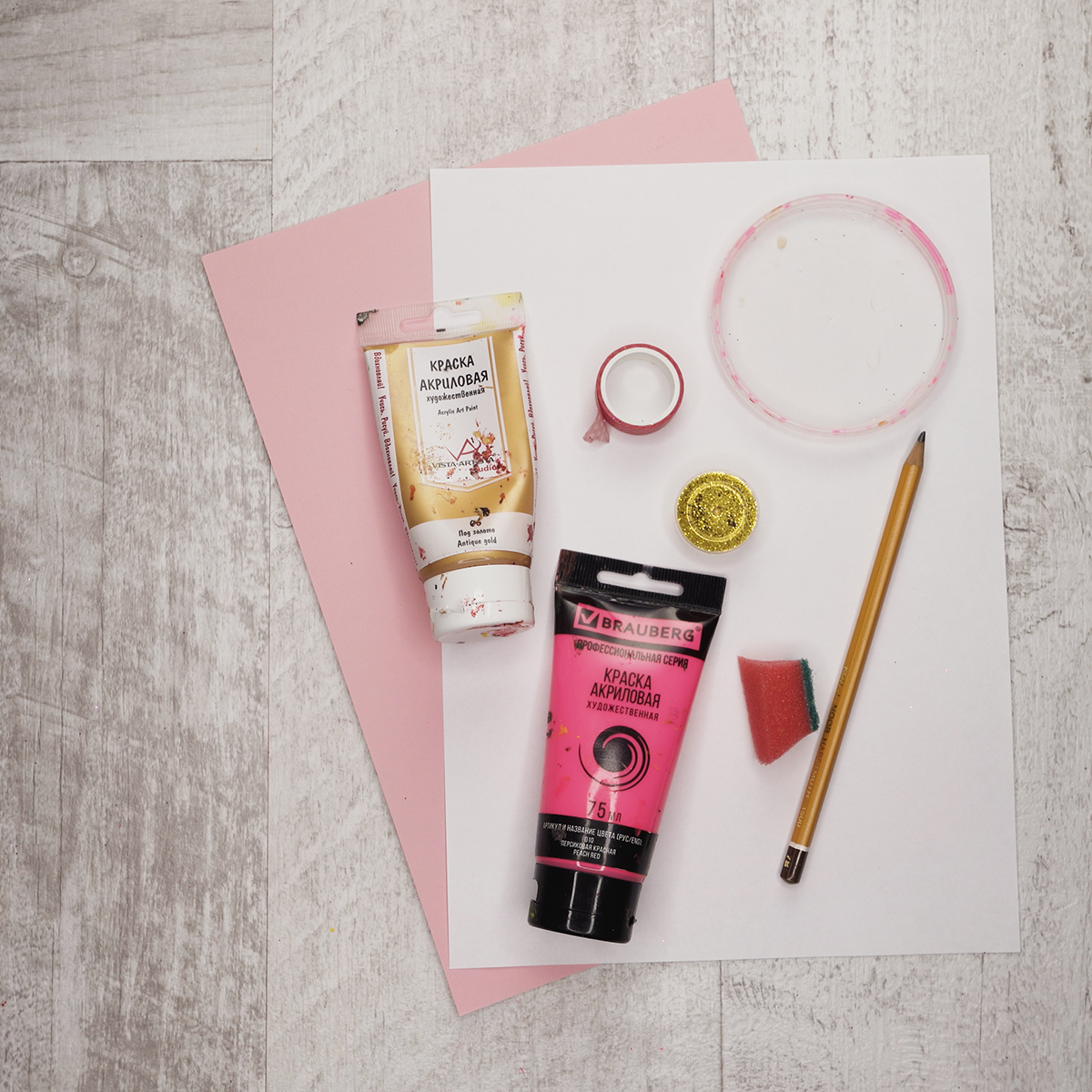 The supplies are pink and white paper, pink and gold paints, some sponge, a pencil and gold glitter