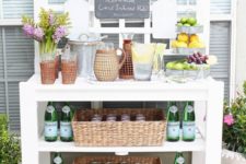 20 an outdoor drink station of a large table with shelves, baskets, vases and a chalkboard menu