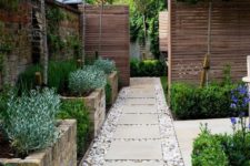 22 a welcoming pathway with large brick flower beds with greenery and pebbles on the ground with large tiles