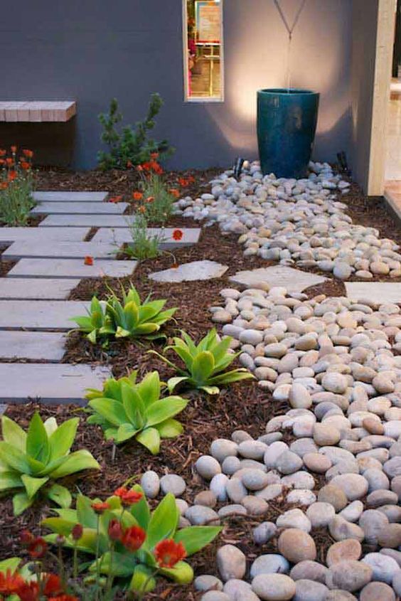 a front yard pathway of tiles lined up with succulents, blooms and large pebbles all around