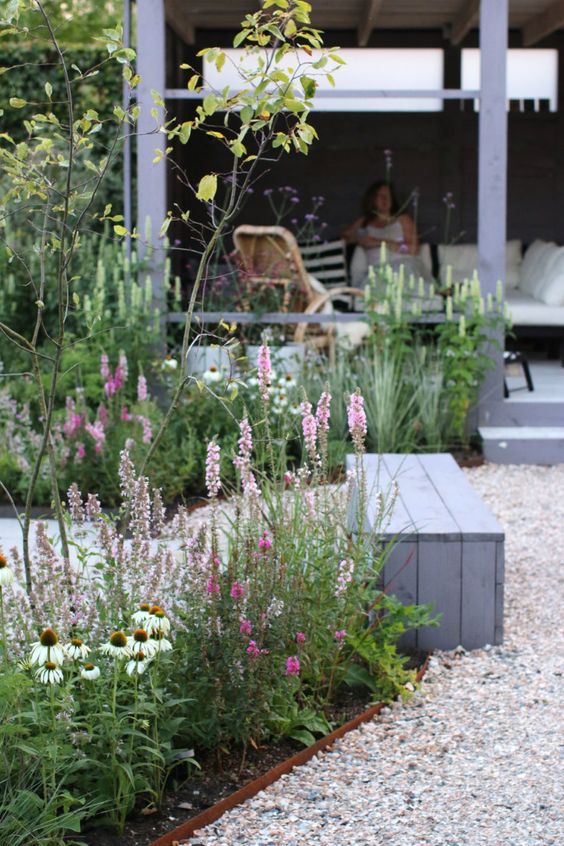 a Scandinavian garden with garden beds with metal edging, blooms and greenery, grey wooden furniture and a gravel path