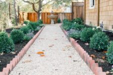 a chic modern garden with a gravel path, garden beds with shrubs and brick edging and a traditional fountain