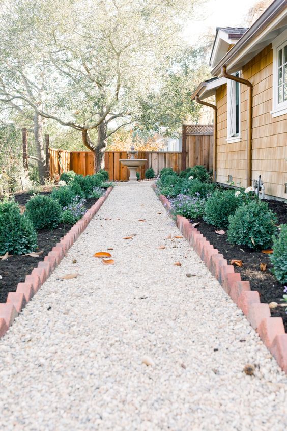 a chic modern garden with a gravel path, garden beds with shrubs and brick edging and a traditional fountain