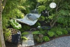 a cool garden nook with lots of greenery, a hammock with pillows, a gravel path with metal edging, a basket with blankets