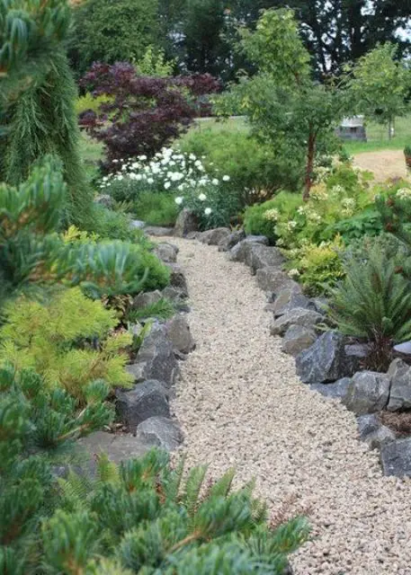 a creative green garden with trees, shrubs, greenery, a gravel pathway with rock edging looks very natural