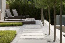 a formal outdoor space with a gravel and long paving stones plus a wooden deck and trees lining the path