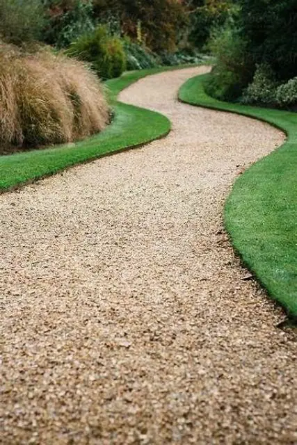 a minimalist garden with a green lawn and a gravel pathway and some shrubs and greenery  is a stylish and edgy idea