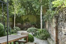 a modern and chic garden with a gravel path, wooden dining set, greenery, shrubs and trees is a lovely and chic space