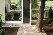 a modern backyard with gravel and concrete stepping stones, a tree and shrubs and a shed for gardening