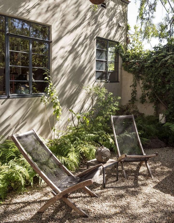 a modern gravel backyard with wooden folding chairs, a side table with decor and some ferns around