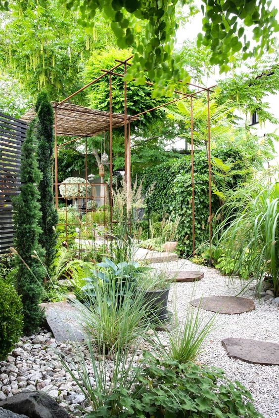 a modern green garden with a lot of greenery and shrubs, gravel and large stones, a little terrace is cool and modern