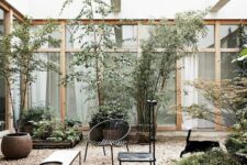 a modern inner yard with gravel on the ground, modern black furniture, a bench, greenery and some trees is chic