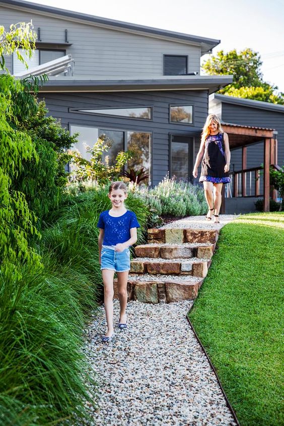 a modern sloping backyard with a green lawn, a gravel pathway and a staircase of stone is a cool idea for a modern space