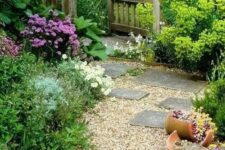 a pretty countryside garden with greenery and blooms, with planters, a gravel pathway and some stone steps