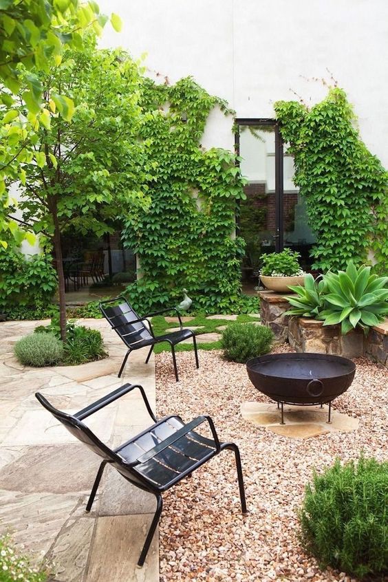 a stylish modern backyard done with gravel and stone, with metal chairs, a fire put, some greenery around is cool
