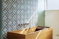 05 a rectangular wooden bathtub on legs looks contrasting with a blue mosaic wall in foront of it