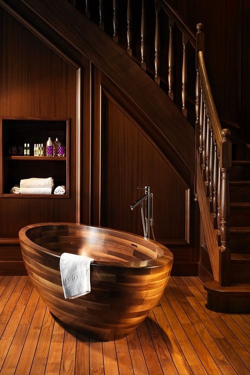 a wooden oval bathtub with metal fixtures looks elegant and chic in a wooden bathroom