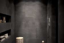 a black bathroom with large and smaller scale tiles, built-in shelves and a tree stump table
