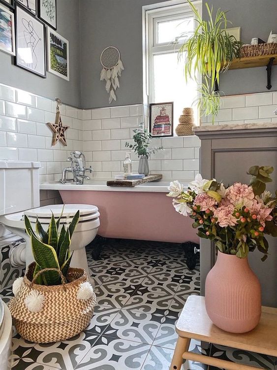 a boho bathroom with grey walls, white subway tiles, a pink tub, printed tiles, a grey vanity, greenery, blooms and decor