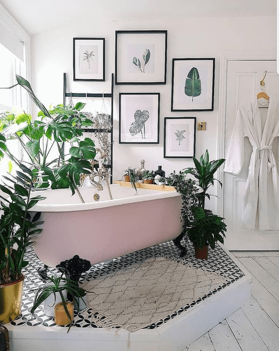 a catchy tropical bathroom with a pink clawfoot tub on a platform, a tropical gallery wall, potted plants and mosaic tiles