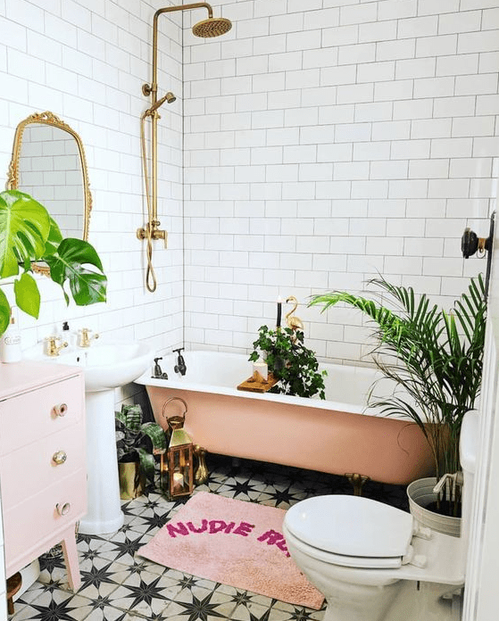 a glam tropical bathroom in neutrals, a pink tub, a pale pink vanity, a pink rug and potted plants, gold touches