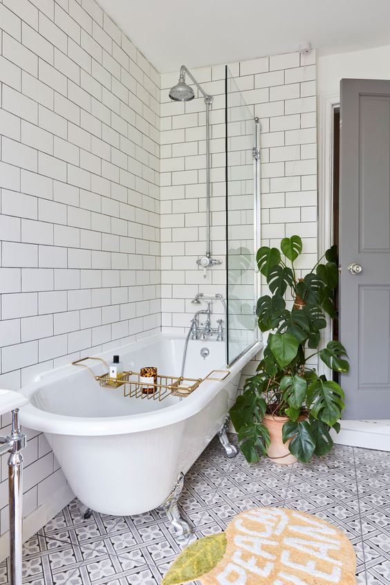 a lovely bathroom with white subway and printed tiles, a clawfoot tub, a bright rug and potted plants is a fun and cool idea
