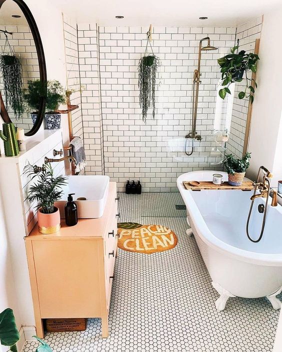 a lovely boho bathroom with subway and penny tiles, a clawfoot tub, a peachy vanity, greenery and a lvoely rug