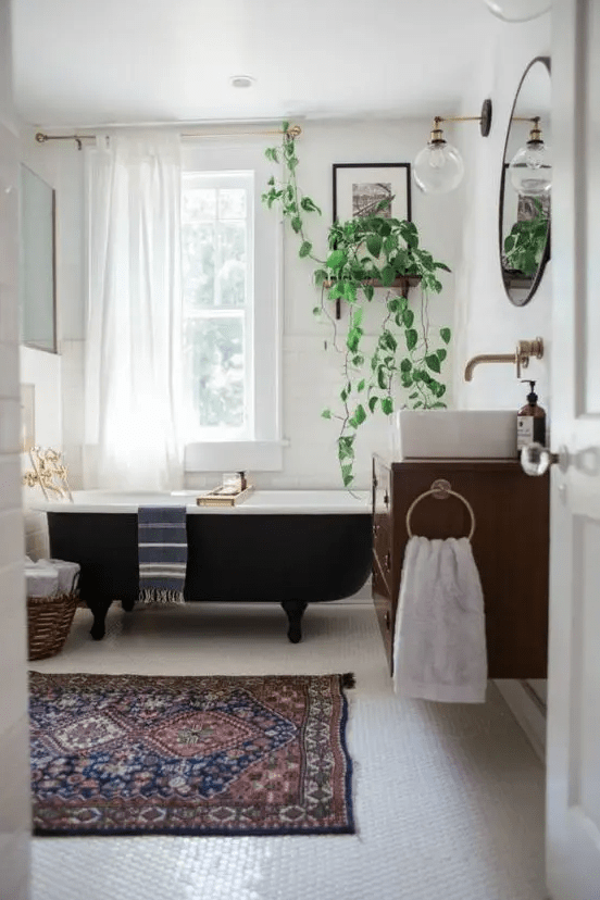 A mid century modern bathroom with white subway tiles and penny ones, with a black clawfoot tub, a floating vanity and potted plants
