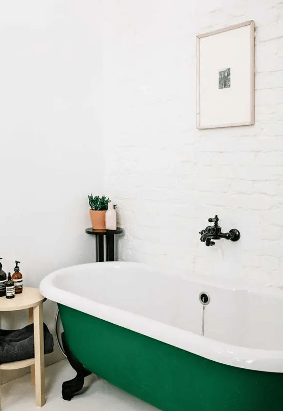 a neutral bathroom with a white brick wall, an emerald clawfoot bathtub, a wooden side table, some potted plants is amazing