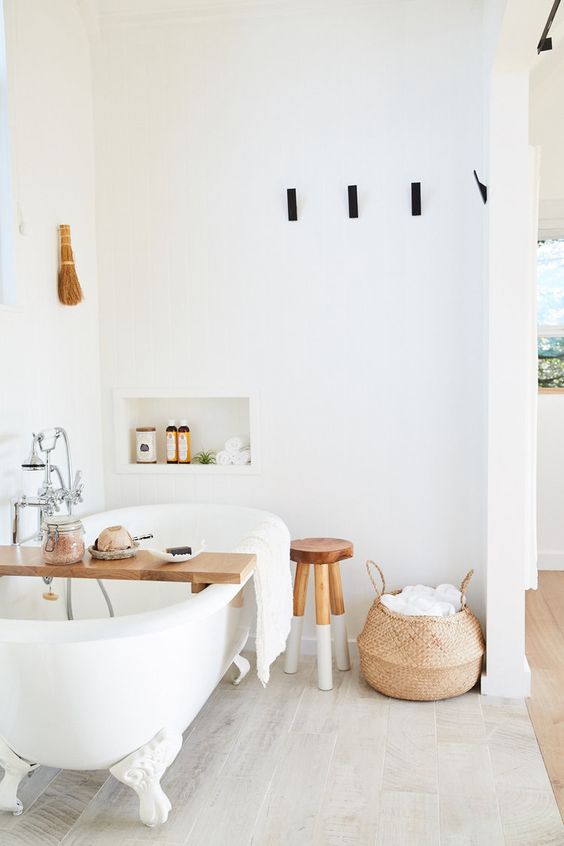 a pure white bathroom with a clawfoot tub, a niche, a stool and a basket with towels is a lovely space to relax in
