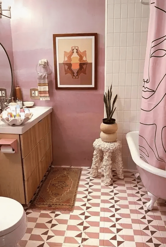 a quirky pink bathroom with geo tiles on the floor, a pink free-standing bathtub and a pink curtain, a light-stained vanity