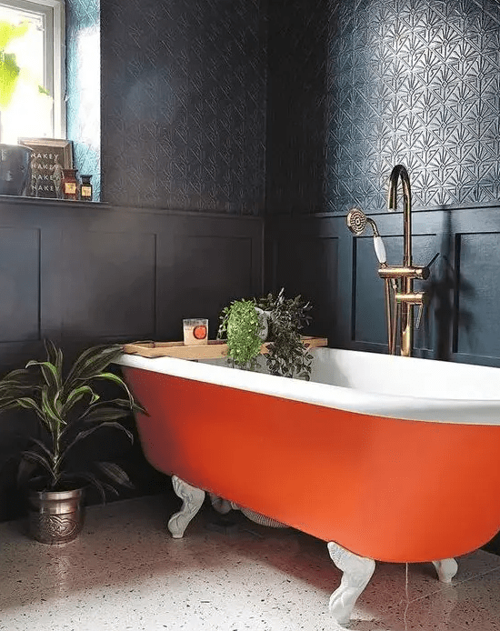 a refined moody bathroom with black walls and paneling, an orange clawfoot bathtub, potted greenery and candles is wow