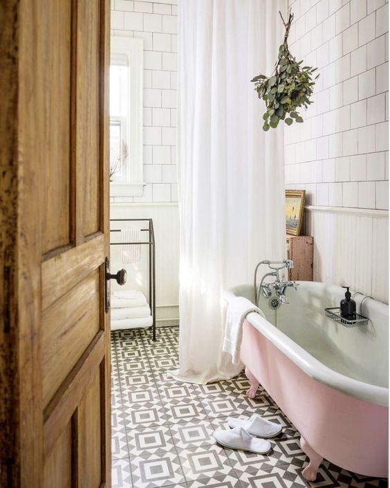 A vintage inspired bathroom with square and printed tiles, a pink clawfoot tub, a vanity and greenery is cool