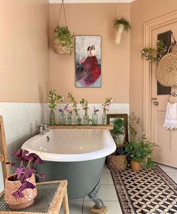 a welcoming bathroom with peachy walls and a door, white subway tiles, a green clawfoot tub, lots of greenery and plants