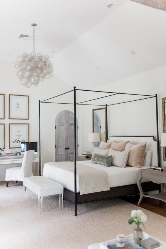 a chic modern farmhouse bedroom with a frame bed, a bench, nightstands, a desk, a gallery wall and a bubble chandelier