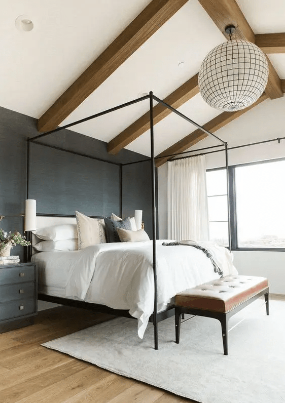 a chic modern farmhouse bedroom with wooden beams, a black grasscloth wallpaper wall, a black frame bed, black nightstands and a leather bench
