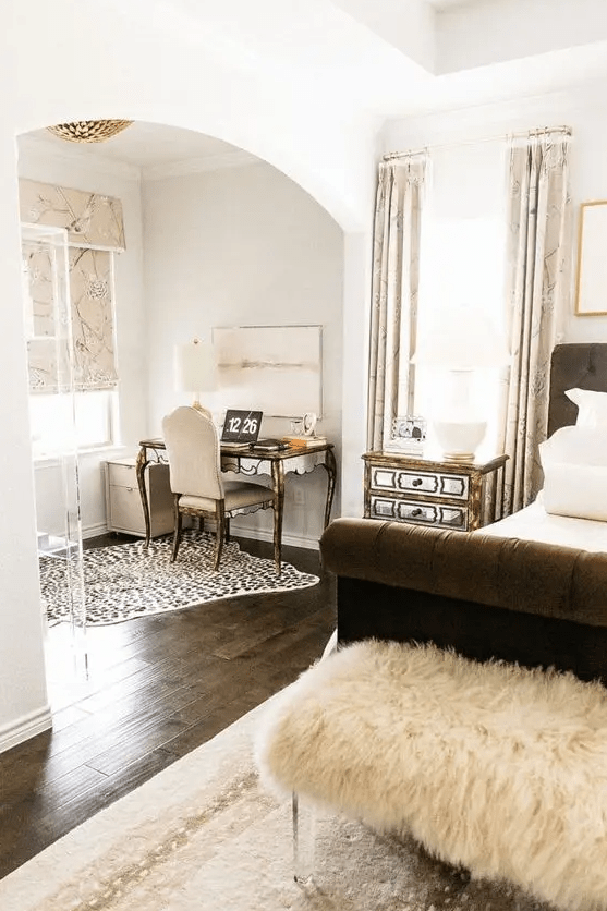 a luxurious bedroom with an alcove home office, a refined vintage desk and a chair, an acrylic stand, a brown bed, a faux fur bench